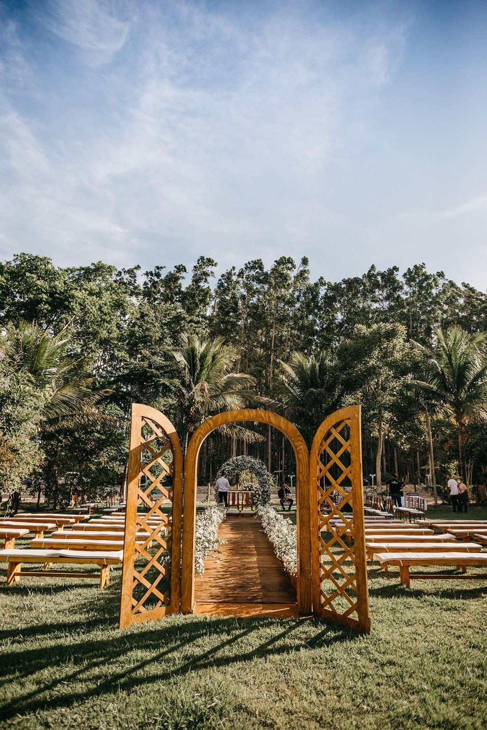 Ceremonia al aire libre con arco de madera y bancas entre palmeras